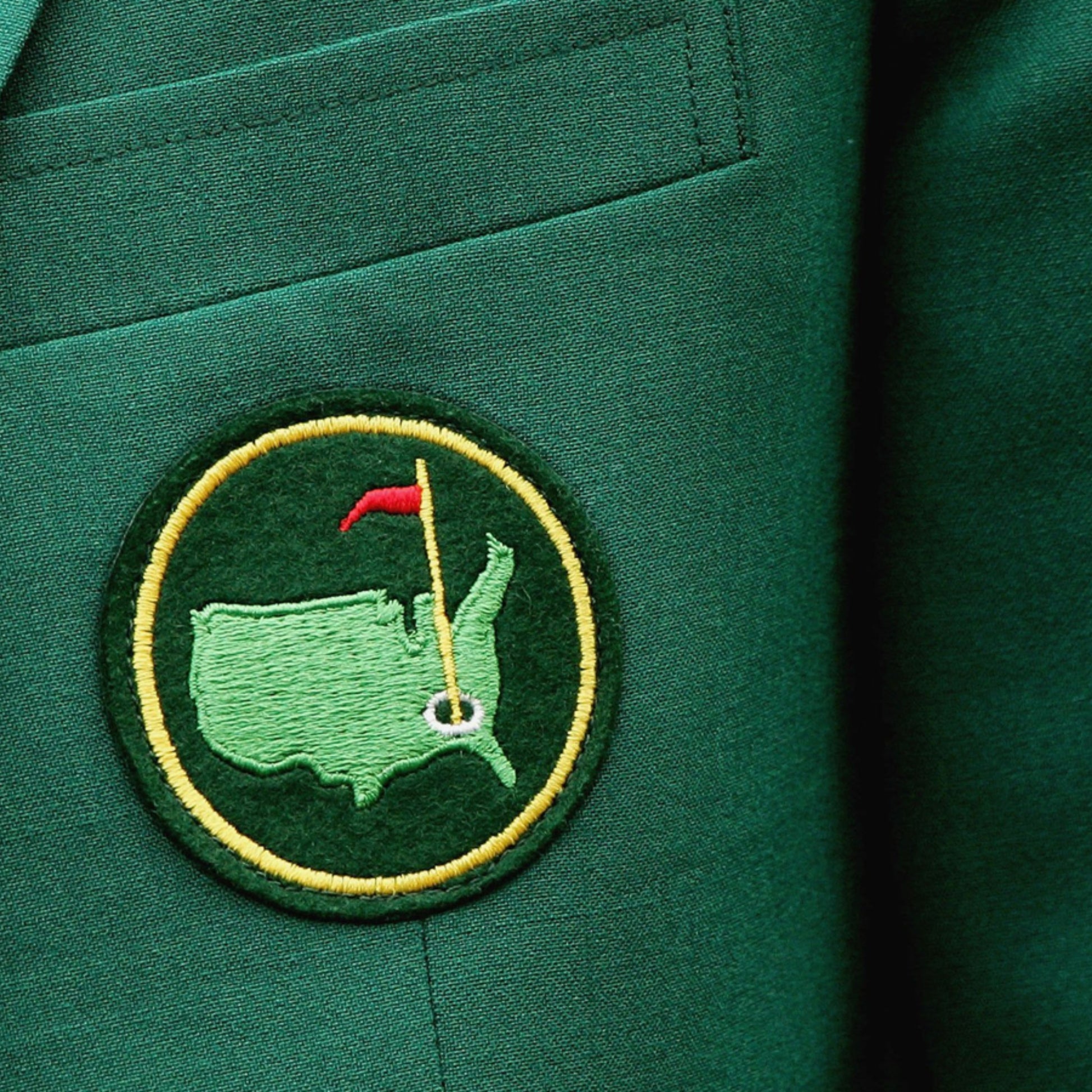 The blazer is a formal jacket, typically associated with prestigious events or organizations. The emblem on the pocket appears to be a map outline with a flag, which is often associated with the Masters Tournament, a major golf championship. 